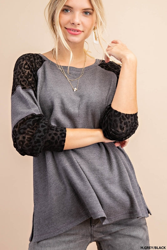 A woman wearing a heather grey thermal long sleeve tee top with black animal print insets on the sleeves.