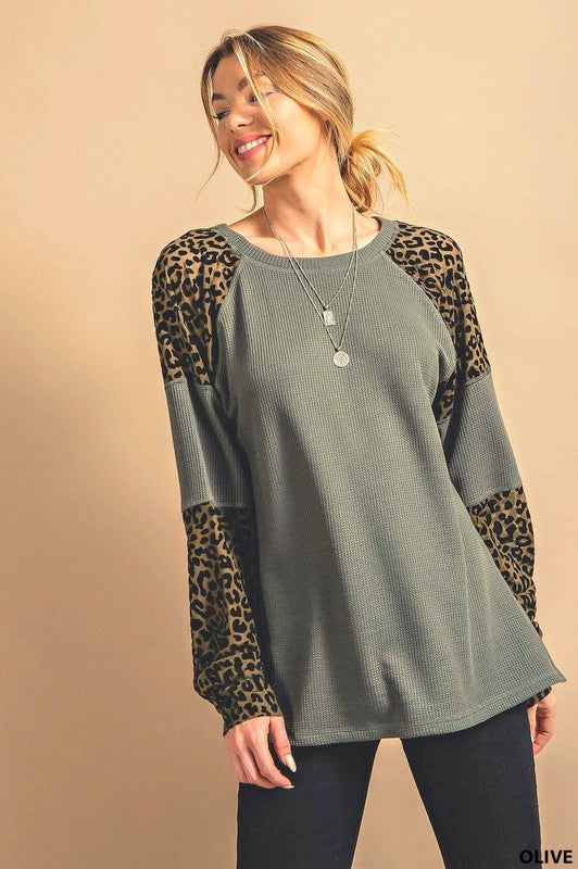 A woman wearing an olive green thermal long sleeve tee top with animal print on the sleeves and a plain olive green background.
