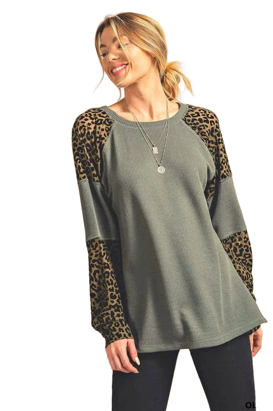 A woman wearing an olive green thermal long sleeve tee top with animal print on the sleeves and a plain olive green background.